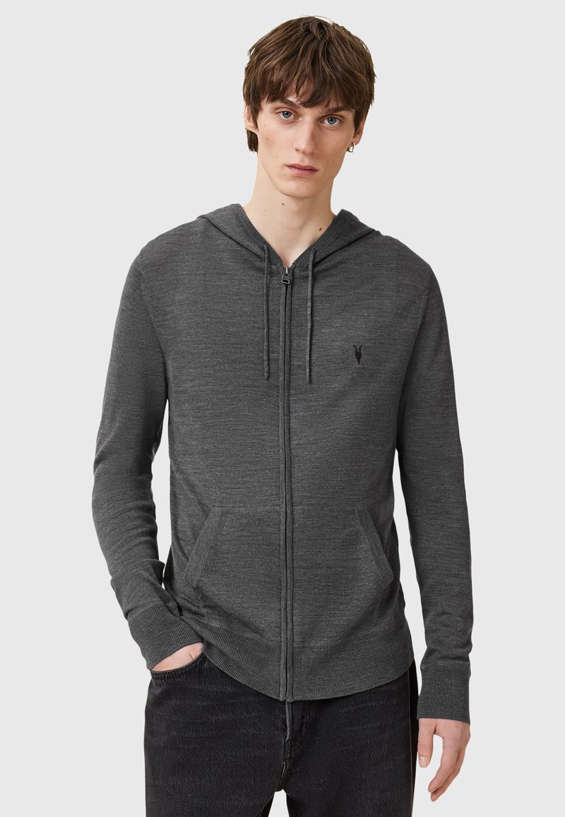 Grå zip-up hoodie tillverkad av mjukt material med en framficka, dragsko i huvan och subtil logotypdetalj på bröstet.