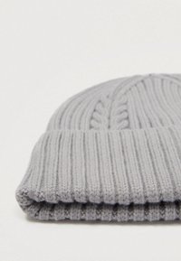 Pelēka adīta ķivere ar rilotu tekst�ūru, kurai ir adījuma dizains pār topu un salocīts malums apakšā.