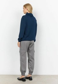 Suéter de cuello alto en navy, de corte relajado, combinado con pantalones cargo grises con puños elásticos y bolsillos laterales, completado con zapatos planos negros.