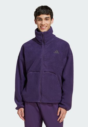 Lila Fleecejacke mit hohem Kragen, Frontreißverschluss und zwei Fronttaschen. Mit einem Logo auf der linken Brust. Weiches, strukturiertes Material.