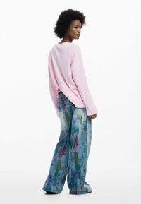 Roosa pikkade varrukatega särk, millel on lõdvestunud lõige, koos laiade sääreosadega teksadega, millel on värvilise värvitilkade muster ja veidi lõdvem lõige.