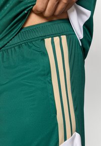 Πράσινα αθλητικά σορτς με υφή, ελαστική μέση και μπεζ κατακόρυφες ρίγες στα πλάγια.