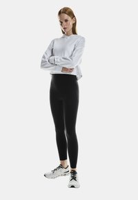 White cropped hoodie, black leggings, and white athletic shoes. Smooth fabric with a relaxed design. Shoes feature black laces and textured soles.