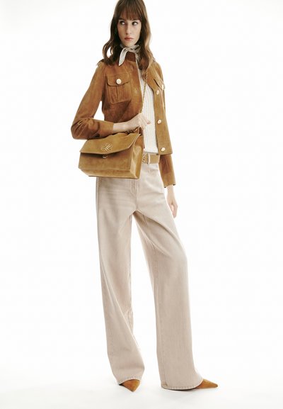 Woman wearing a brown suede jacket, beige knit top, wide beige pants, pointed brown shoes, and carrying a matching brown suede handbag.