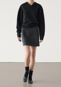 Ciemnoszara, oversize'owa, dziana sweter z dekoltem w serek, w połączeniu z dopasowaną, szaro-skalną spódnicą. Modelka nosi czarne skarpety i baleriny z ćwiekami.