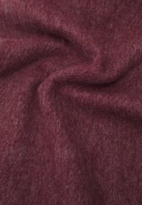 Tissu en laine marron foncé avec une surface douce et légèrement texturée, présentant des variations subtiles de teinte et une forme organique drapée.