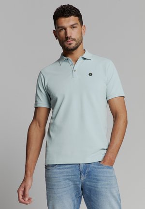 Lichtblauw poloshirt van zachte katoen, met een drieknoopsluiting en een klein hexagonaal logo op de linkerkant van de borst. Korte mouwen.