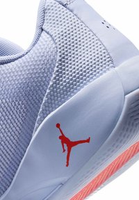 Helleblaue Sportschuh mit einem strukturierten Obermaterial aus Stoff, einem roten Jumpman-Logo und einer gemusterten Sohle mit einem orangefarbenen Akzent.