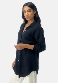 Camicia nera con bottoni, realizzata in un tessuto strutturato e stropicciato, presenta un colletto e maniche lunghe. Ha una vestibilità rilassata con orlo arrotondato.