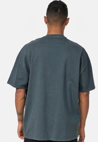 Bavlněné oversized šedé tričko s krátkým rukávem, žebrovaným límcem a uvolněným střihem. Má hladkou texturu a žádné viditelné vzory či akcenty.