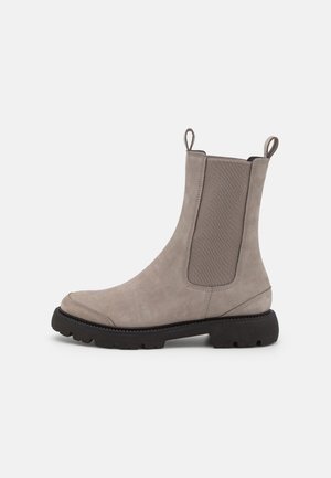 Beżowy zamszowy botek za kostkę z elastycznymi panelami po bokach i pętelkami do ściągania, wyposażony w grubą czarną gumową podeszwę i zaokrąglony czubek.