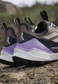 Para czarno-fioletowych butów do biegania trail Adidas Terrex na skalistym terenie, z widocznymi pętelkami na pięcie.