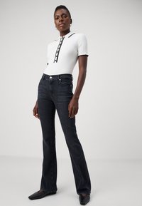 Haut blanc côtelé avec des accents noirs, manches courtes et patte de boutonnage, associé à un jean en denim foncé à jambes évasées et des chaussures noires à bout pointu.