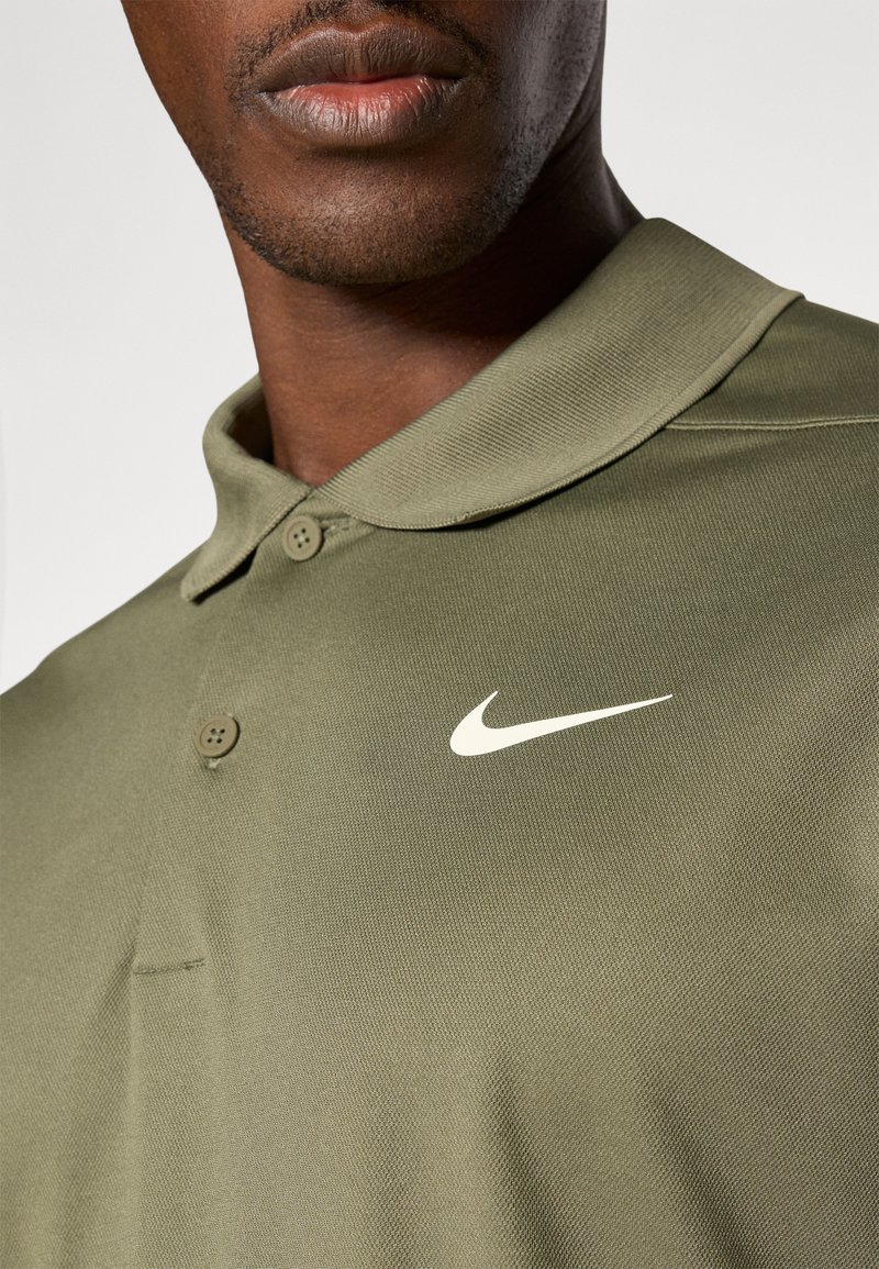 Polo vert olive en tissu texturé, avec un col à deux boutons et un logo Nike swoosh blanc sur la partie gauche de la poitrine.