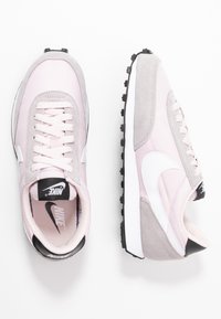 Nike sneakers med en rosa tyg- och gråmocka övre del, vita detaljer, svart sula och klassisk snörningsdesign.
