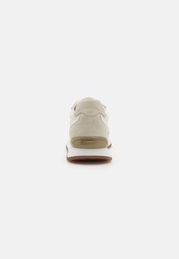 Baskets grises claires avec un dos en suède, un corps en mesh blanc, une semelle en caoutchouc et un branding bien visible à l'arrière. Design minimaliste et forme épurée.