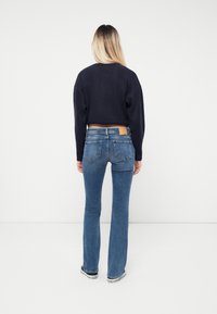 Marinblå kortad tröja, blå utsvängda jeans och svarta sneakers. Jeansen har en bakficka och subtila blekningar. Enkel, avslappnad design.