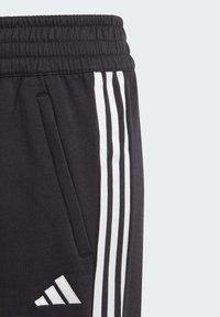 Pantalons de sport noirs avec des rayures blanches sur les côtés, taille élastique et un petit logo sur la jambe inférieure. Dispose de poches latérales et d'une texture douce.