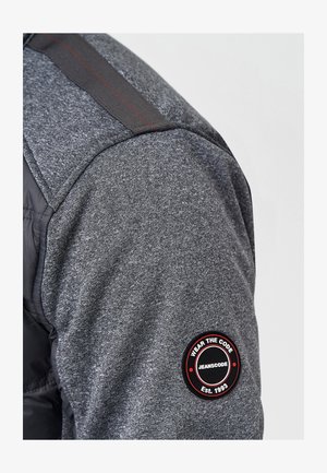 Grijze sweatshirt van een textuurstof, met een ronde merkpatch op de mouw met rode accenten en een zwart zijpaneel.