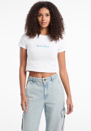 T-shirt blanc court avec logo turquoise "Guess Jeans", associé à un pantalon en denim taille haute bleu clair, doté de poches et d'une coupe décontractée.
