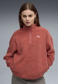 Pullover in pile di colore rosa cipria, con colletto alto, chiusura a mezza zip e un piccolo logo bianco sul petto. Tessuto morbido e strutturato.