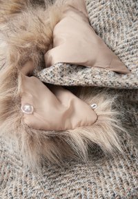 Ljust brunt houndstooth-tyg med mjukt beige foder och konstpälsdetaljer. Innehåller en genomskinlig knapp och texturerade detaljer.