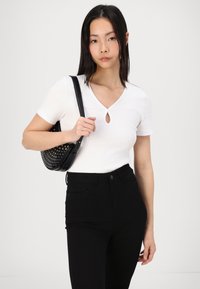 Witte aangesloten top met een sleutelgatdetail, gecombineerd met hoge zwarte jeans en een gestructureerde zwarte schoudertas met ronde gaten.