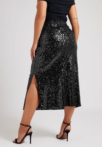 Svart paljett-midi kjol med en sidoslits, som har en åtsittande midja och en slät textur. Bärs ihop med svarta högklackade sandaler.