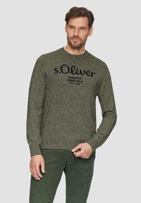 Groene gebreide trui met een ronde halslijn en de tekst "s.Oliver" met "ELEVATED ESSENTIALS SINCE 1968" in donker marineblauw. De textuur lijkt zacht te zijn.