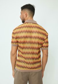 Polo à manches courtes avec un motif en zigzag dans des tons de marron, orange et jaune ; comprend un col beige et des finitions marron.