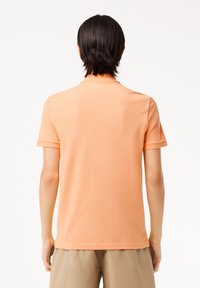 Polo de manga corta en tejido naranja claro con acabado texturizado, que presenta un cuello clásico y mínimos detalles de costura.