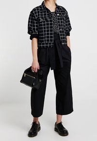 Giubbotto di jeans nero con motivo a griglia bianca, top nero, pantaloni neri a gamba larga e borsa nera. Scarpe nere con suola spessa.
