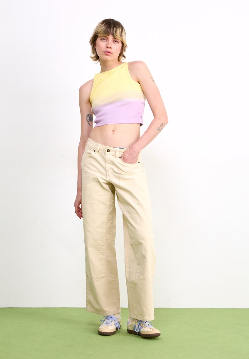 Kort geribd tanktop in gele en paarse kleurverloop; soepelzittende crèmekleurige broek; lichte schoenen met blauwe veters; minimalistisch design.