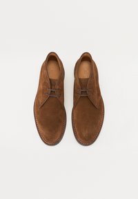 Bruine suède schoenen met een gladde textuur, ronde neus en leren veters. Beschikt over een tan leren binnenzool en contrasterende stiksels op de zool.