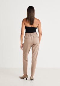Beżowe, dopasowane spodnie z elastycznym pasem, z dwoma tylnymi kieszeniami. W połączeniu z metalicznymi butami na obcasie. Gładka, lekka tkanina.