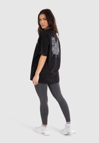 Sort oversized t-shirt med et hvidt fingeraftryksdesign på ryggen, parret med grå leggings og hvide sneakers. Glat stoftekstur.