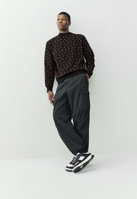 Maglione nero con motivo arancione, pantaloni cargo grigi larghi e sneakers bianche e nere. Design moderno con vita e polsini elasticizzati.