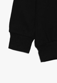 Manica di felpa nera con polsino a coste, caratterizzata da una texture di tessuto liscia e da un design leggermente arricciato nella cucitura della spalla.