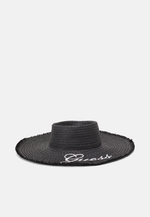 Czarny, szerokokrawędziowy pleciony kapelusz ze słomy z płaską koroną i białym kursywnym logo „Guess” na krawędzi ronda.