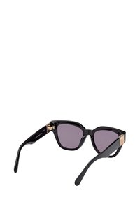 Gafas de sol de estilo cat-eye en color negro con lentes oscuros y detalles en dorado en las patillas, anguladas para mostrar el interior de una de las varillas.