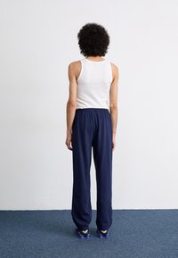Marineblå joggebukser med elastisk midje, sammen med en hvit tanktopp, sett fra baksiden. Har avslappet passform og uformelt design.