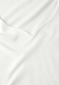 Tessuto bianco che mostra una consistenza morbida e liscia con leggere pieghe e ondulazioni. Il materiale leggero appare traspirante e ha un colore uniforme.