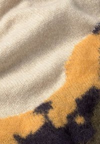 Il tessuto lavorato a maglia presenta sezioni di crema, giallo e verde scuro, con texture variabili e una sensazione morbida, mettendo in mostra una fusione di colori e motivi.
