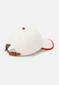 Baseballpet in crèmekleurige katoen met rode accenten op de rand en knop. Voorzien van een verstelbare leren band in bruin met gouden hardware.