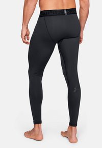 Schwarze Sportleggings mit einem figurbetonten Design, aus glattem Material gefertigt, ausgestattet mit einem breiten Bund, auf dem der Markennamen und ein dezentes Logo an der Seite zu sehen sind.