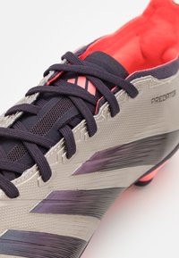 Scarpa da calcio grigia con tomaia testurizzata, dettagli rosa e decorazioni a strisce multiple. Presenta lacci e un interno imbottito per il comfort.