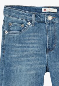 Jeans de mezclilla azul claro con una cintura estándar, bolsillos frontales y herrajes en tono plateado. Presenta una etiqueta con el texto "Levi's Bermuda".