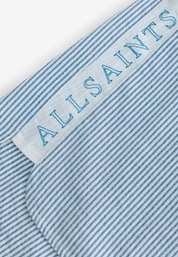 Plavo-bijela tkanina sa prugama i glatkom teksturom. Sadrži etiketu s natpisom "ALLSAINTS" u plavom slovima na bijeloj pozadini.