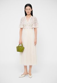 Rochie vaporoasă, de culoare bej deschis, cu broderie florală și mâneci din dantelă; asortată cu o geantă mică verde și pantofi albi cu vârf ascuțit.