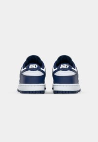Navy and white Nike sneakers featuring a smooth leather upper, padded collar, and rubber sole with grip patterns, viewed from the rear.